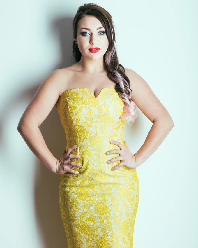 Studio fashion photo of woman in yellow dress against white wall