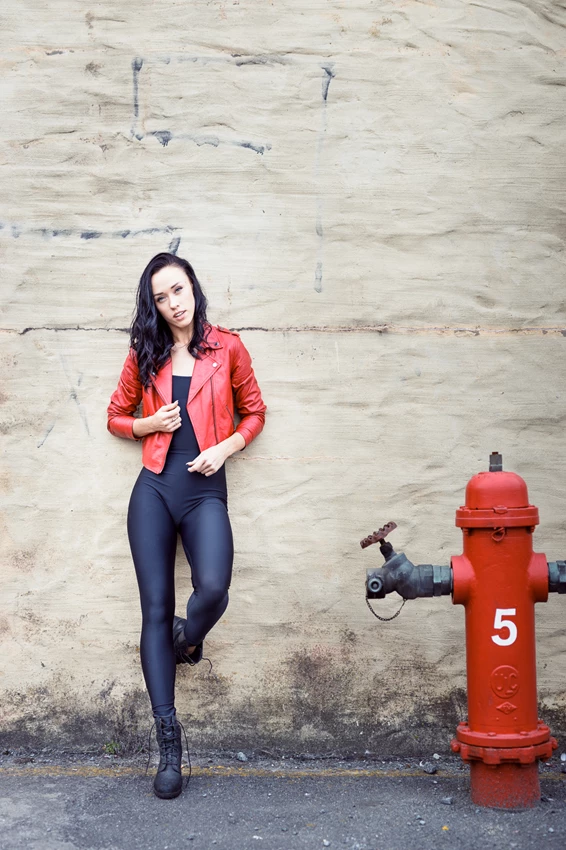 Fashion photo of woman in red leather jacket against wall next to fire hydrant