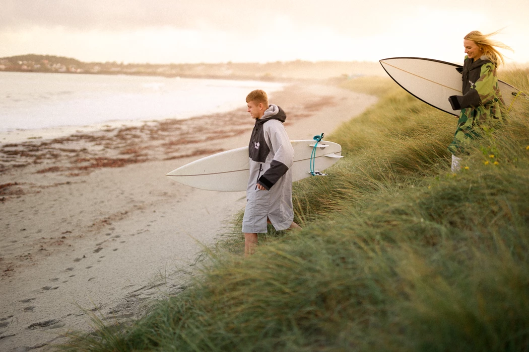 Colour photo of a couple of people walk down a beach with surfboards